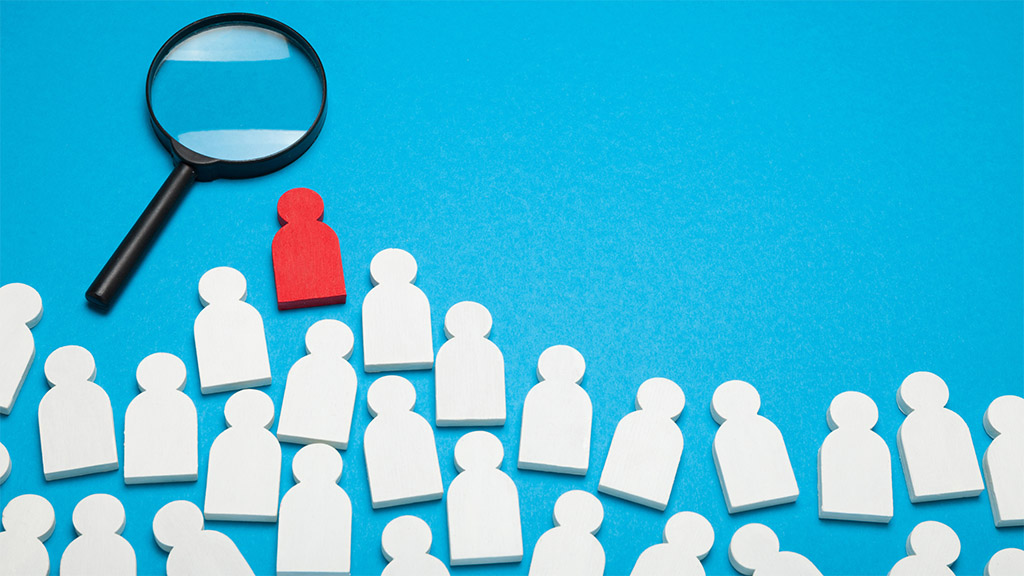 A magnifying glass on a blue background with people icons that are white in color with one that is red.